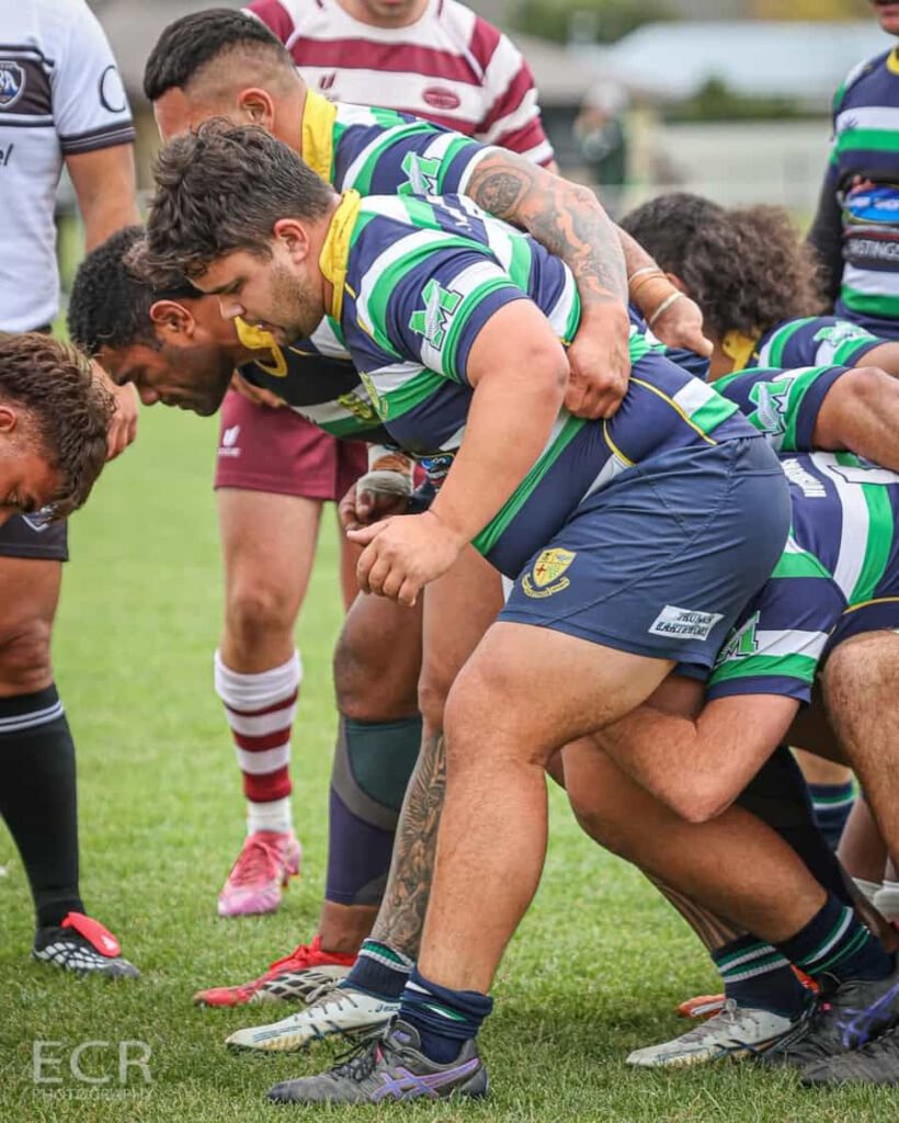 Rugby players in green and blue jerseys binding together in a scrum